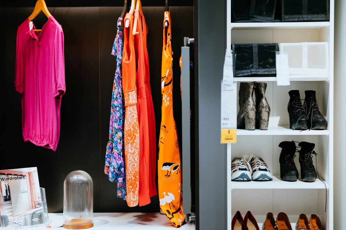 Pink, orange and floral dresses hanging on a rail in a small shop, with shoes on the shelves beside them.