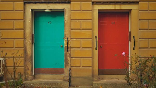 Two doors side by side in a yellow wall, one teal and one red.