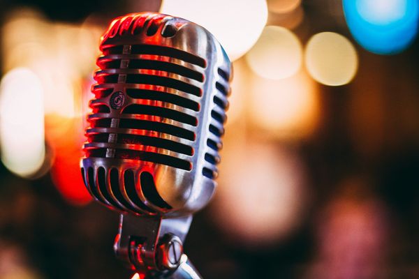 A chrome microphone on a stand, lit warm against soft bokeh lights.
