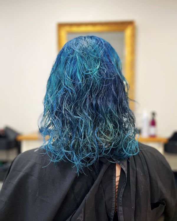 Mes cheveux vus de dos dans un salon de coiffure/coloration, ils sont bleus avec des reflets plus sombres, et des ondulations fines et des légères boucles.