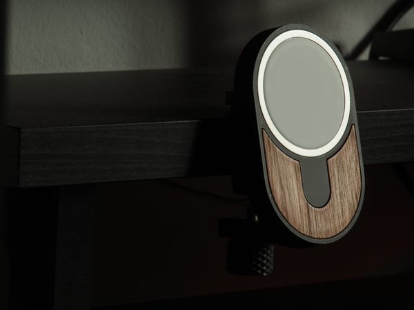 Photo of a black MagSafe Holder with a natural wood accent on the front, clamped on a black desk shelf.