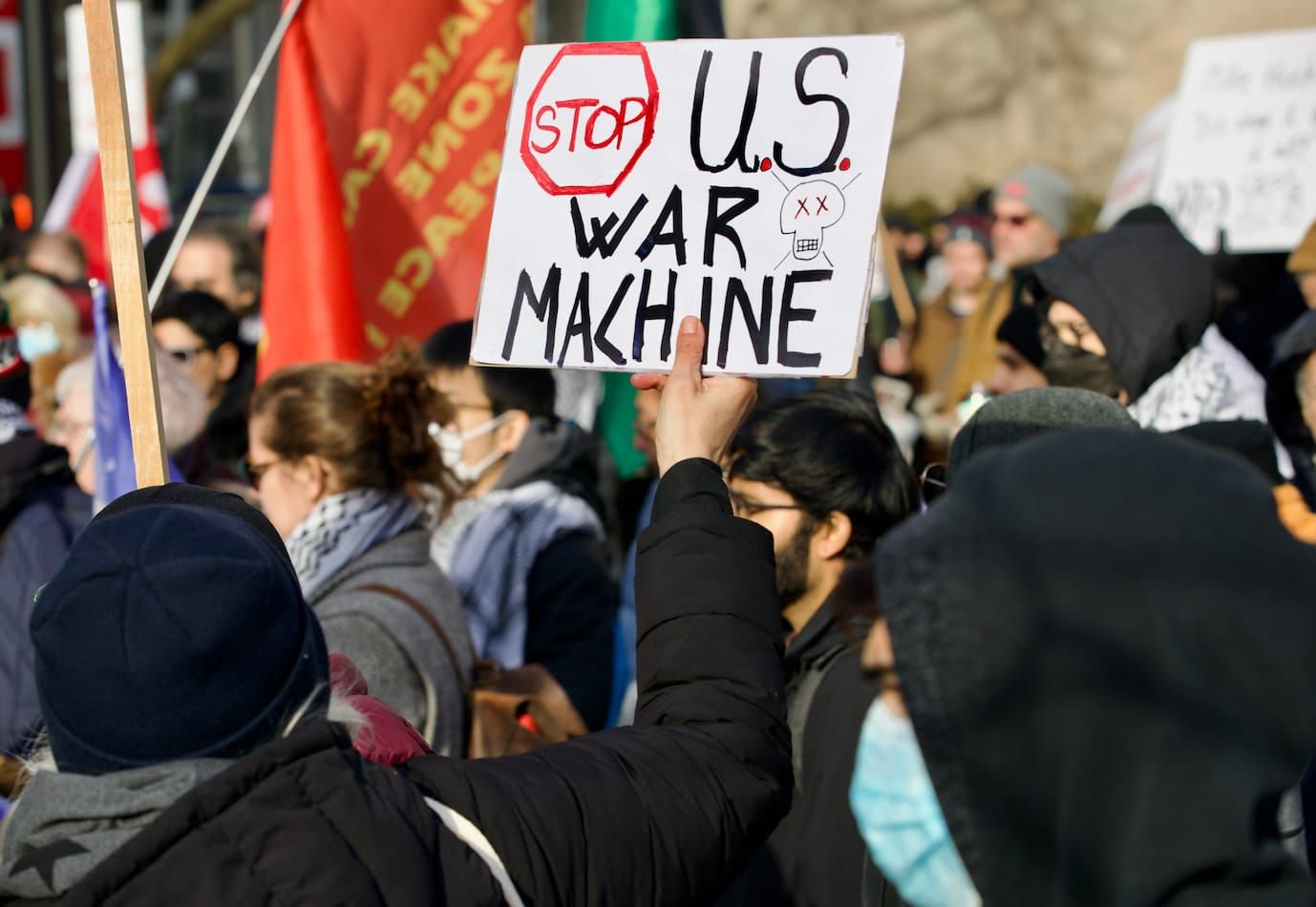 A person at a protest holding a sign saying "Stop U.S. War Machine"