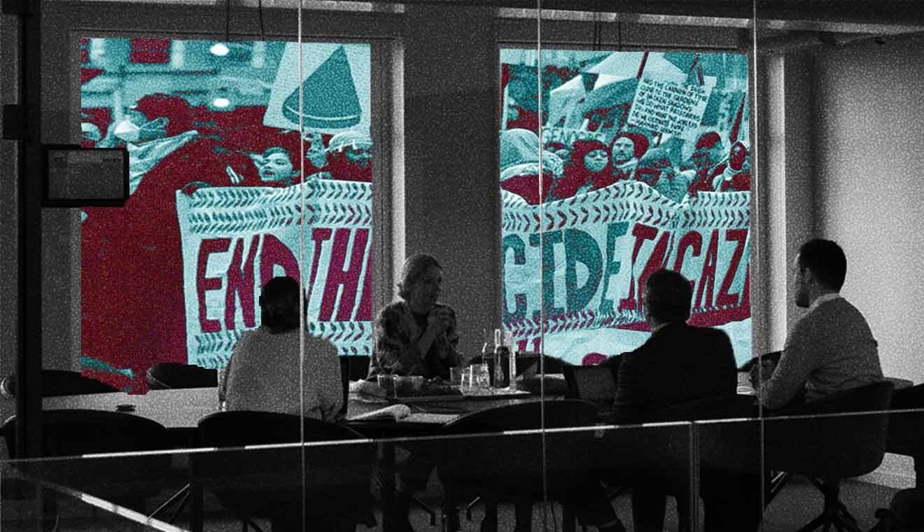 People gathered for a meeting with protest signs seen in the windows.