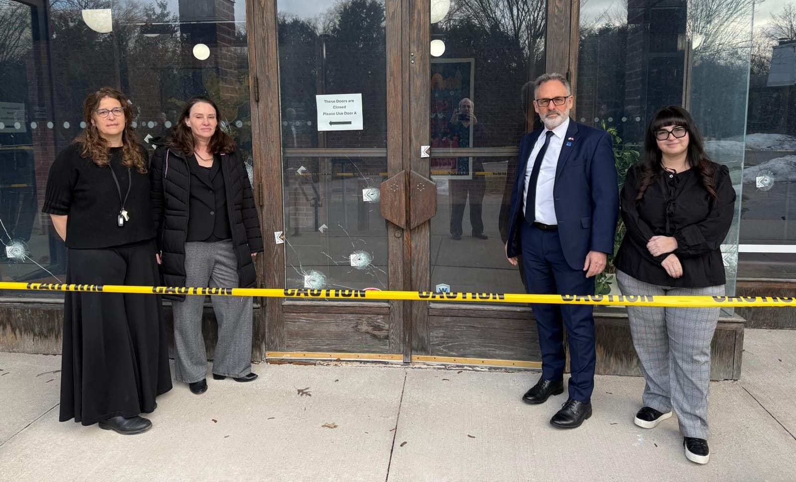 People stand in front of a synagogue with several bulletholes in the glass