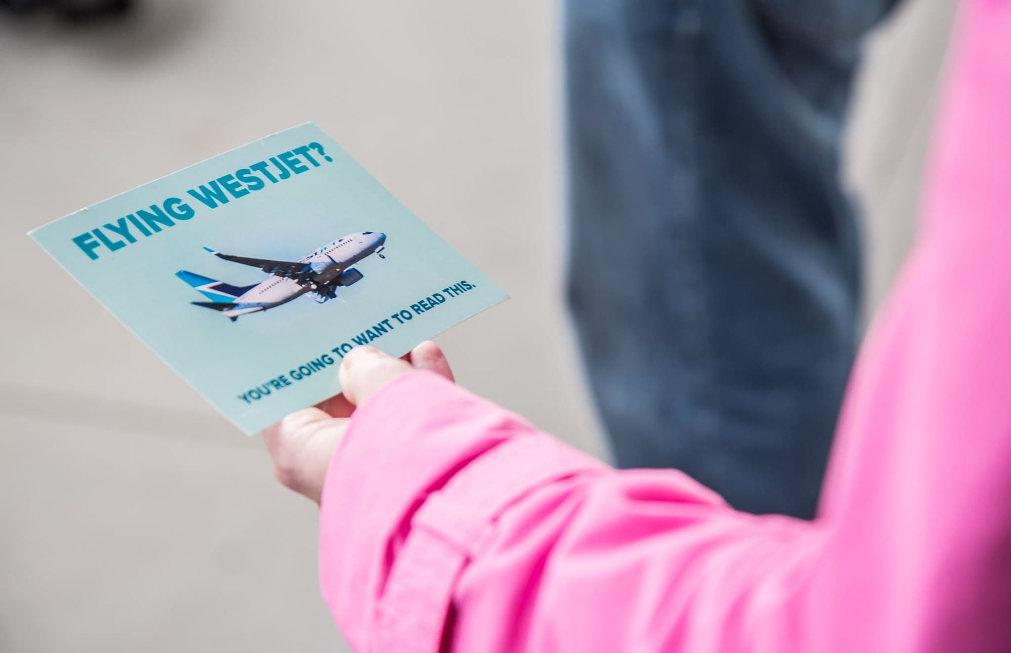 Person holding a card saying "Flying Westjet? You're going to want to read this."