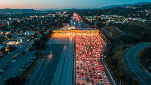 8-lane highway at dusk, all lanes converging into a single toll booth creating a massive traffic backup