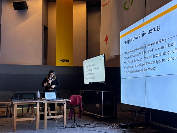 Ja stojąca z mikrofonem i wyświetlonym slajdem prezentacji