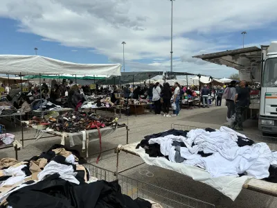 Mercato settimanale popolare con bancarelle di abiti e oggetti usati sotto un cielo mediterraneo