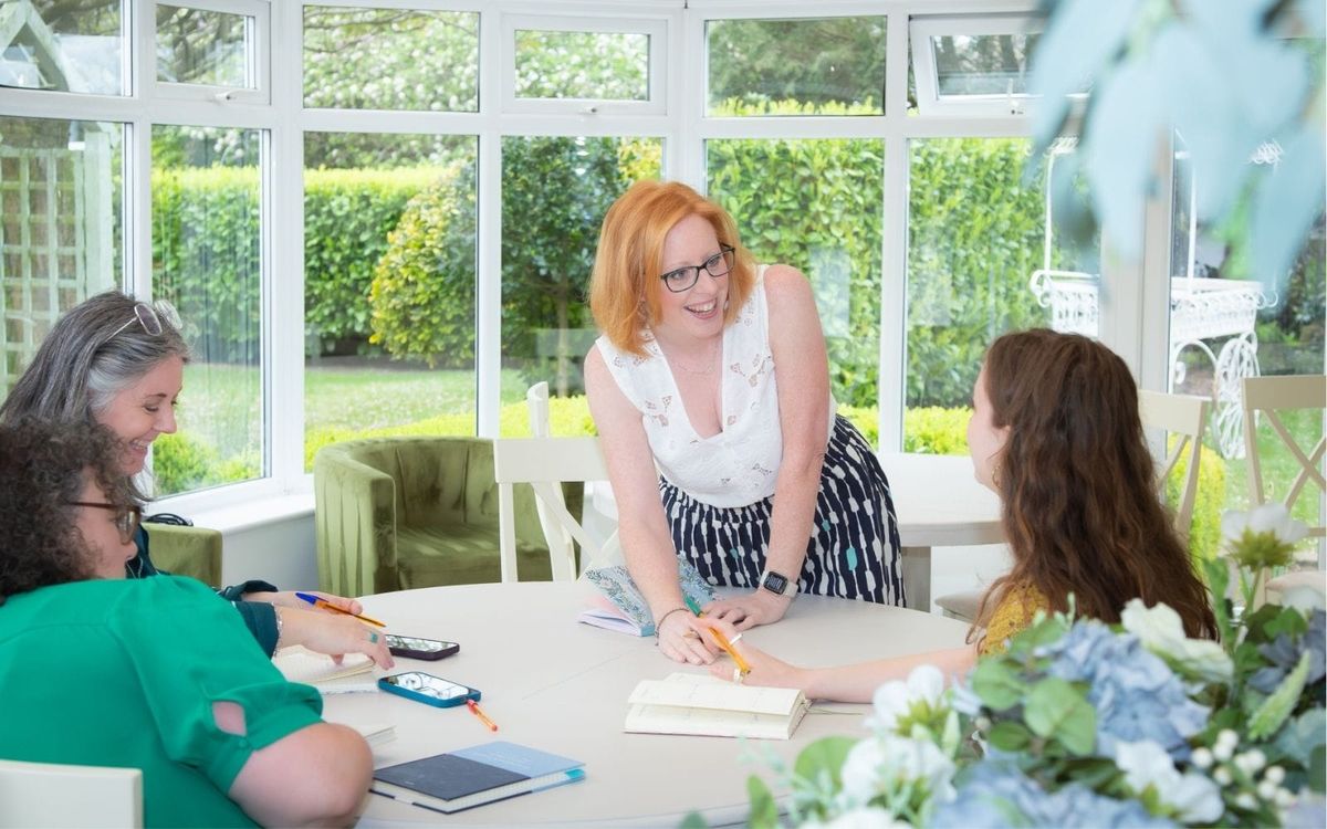 Lucy Davies, business coach, smiling as she leans over a table talking with three women who are taking notes