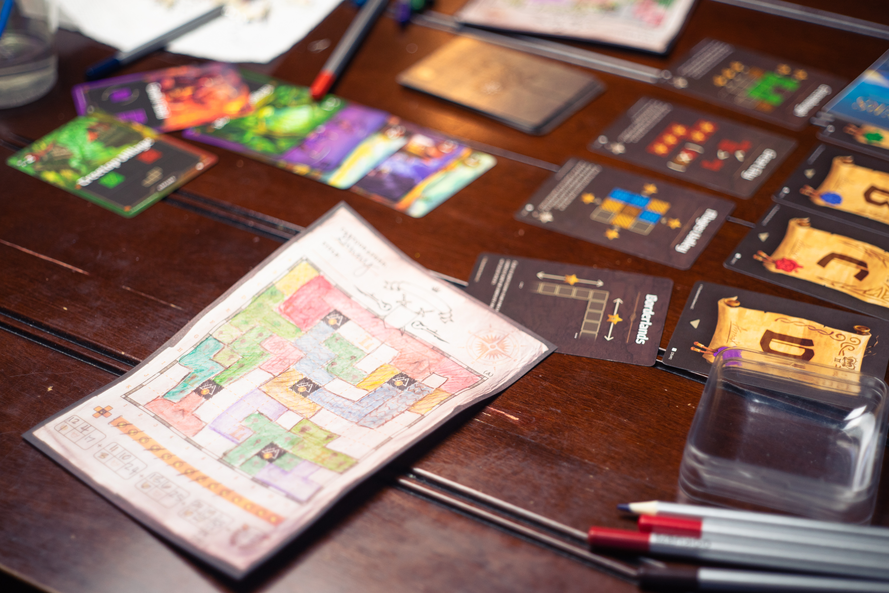 A player sheet, colored pencils, and cards from the game Cartographers.