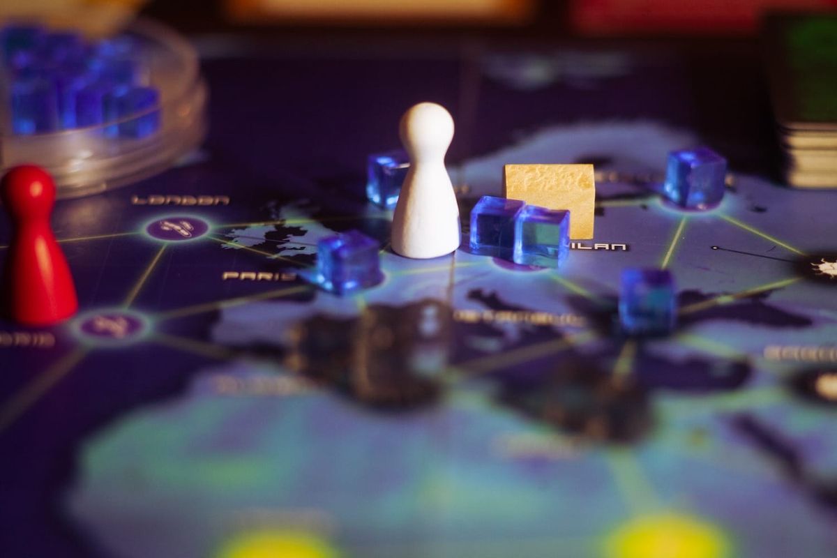 A white pawn on a dark blue board surrounded by blue disease cubes in the board game Pandemic.