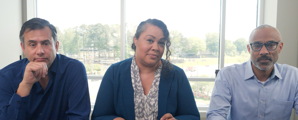 Three people sitting at a table in front of windows