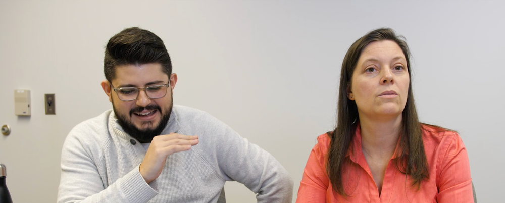 A Latine man and a White woman sitting next to each other at a desk