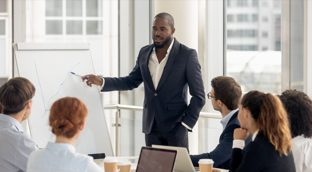 Man leading a work presentation; diverse colleagues listen