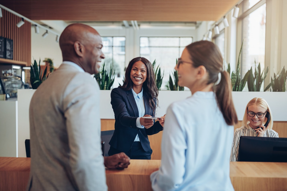 Friendly young African American concierge working at a reception counter giving room information to two guests 