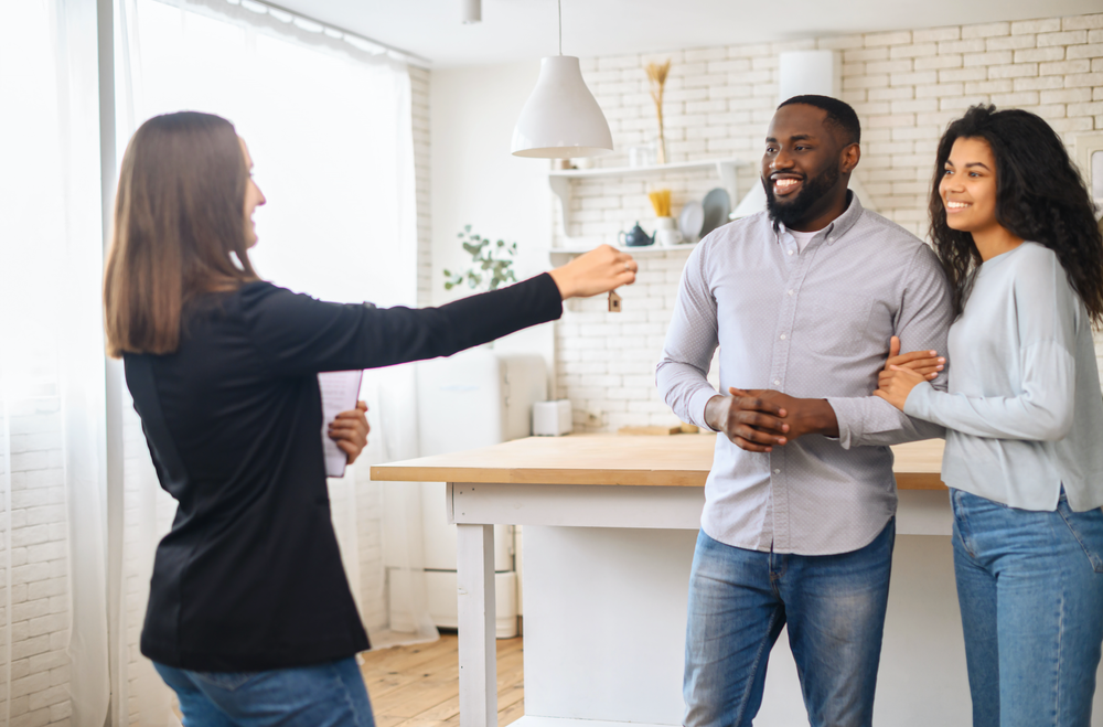 A smiling multiracial couple receives the keys to a new home from a real estate agent