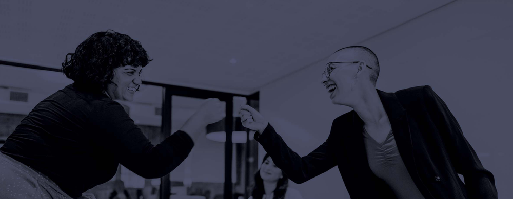 Two people in professional dress fist-bumping and smiling