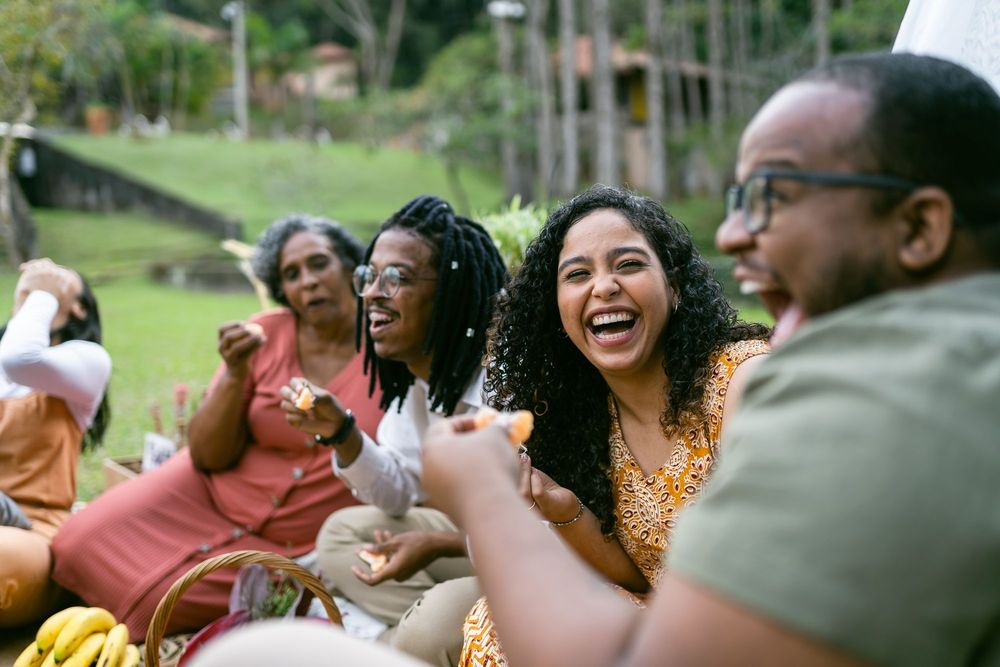 Four individuals of African descent eating outside in a green park