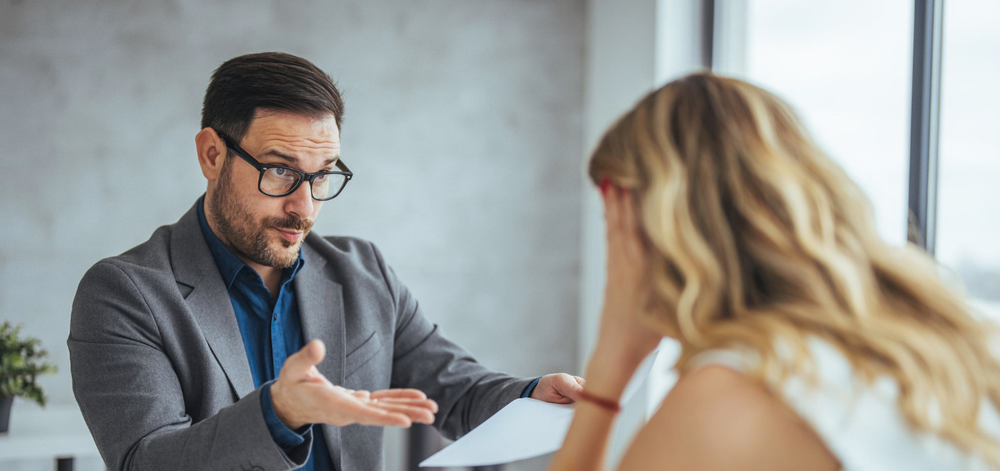 White man gestures skeptically towards a blond person with long hair