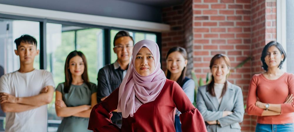 A woman wearing a hijab stands in front of colleagues all looking at the camera