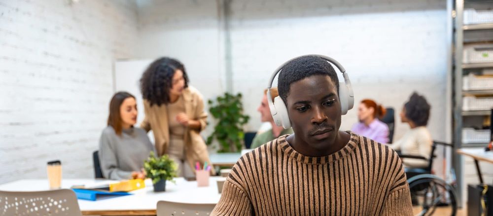Black man in a gold sweater wearing white over-the-ear headphones in front of a blue laptop