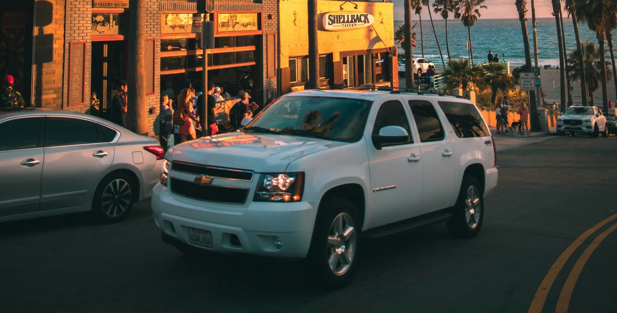 white Chevrolet Tahoe running near parked vehicles