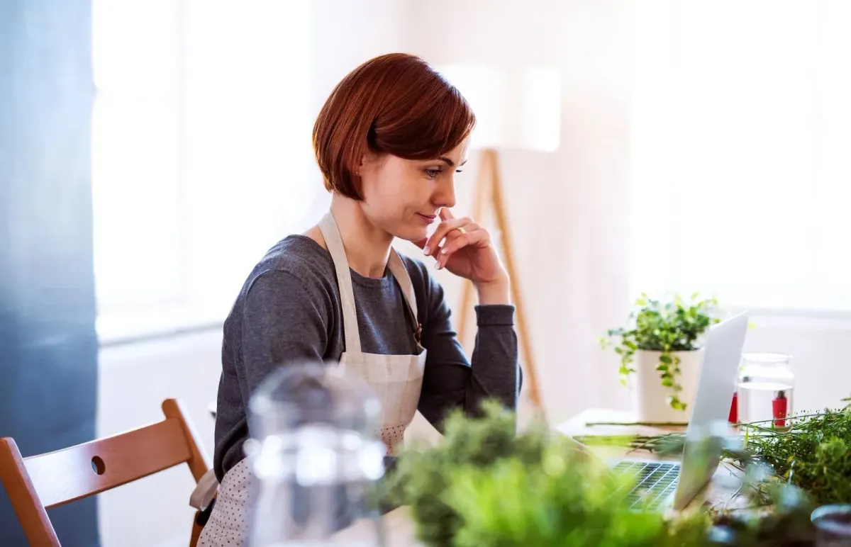 Florist reviewing business numbers on a laptop in a bright studio.