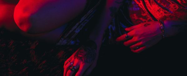 Someone's hands and leg in red light, wearing a red velvet dress, rings and a bracelet
