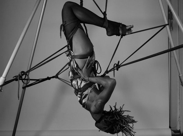 An image of someone suspended upside down from shibari ropes, holding their hips