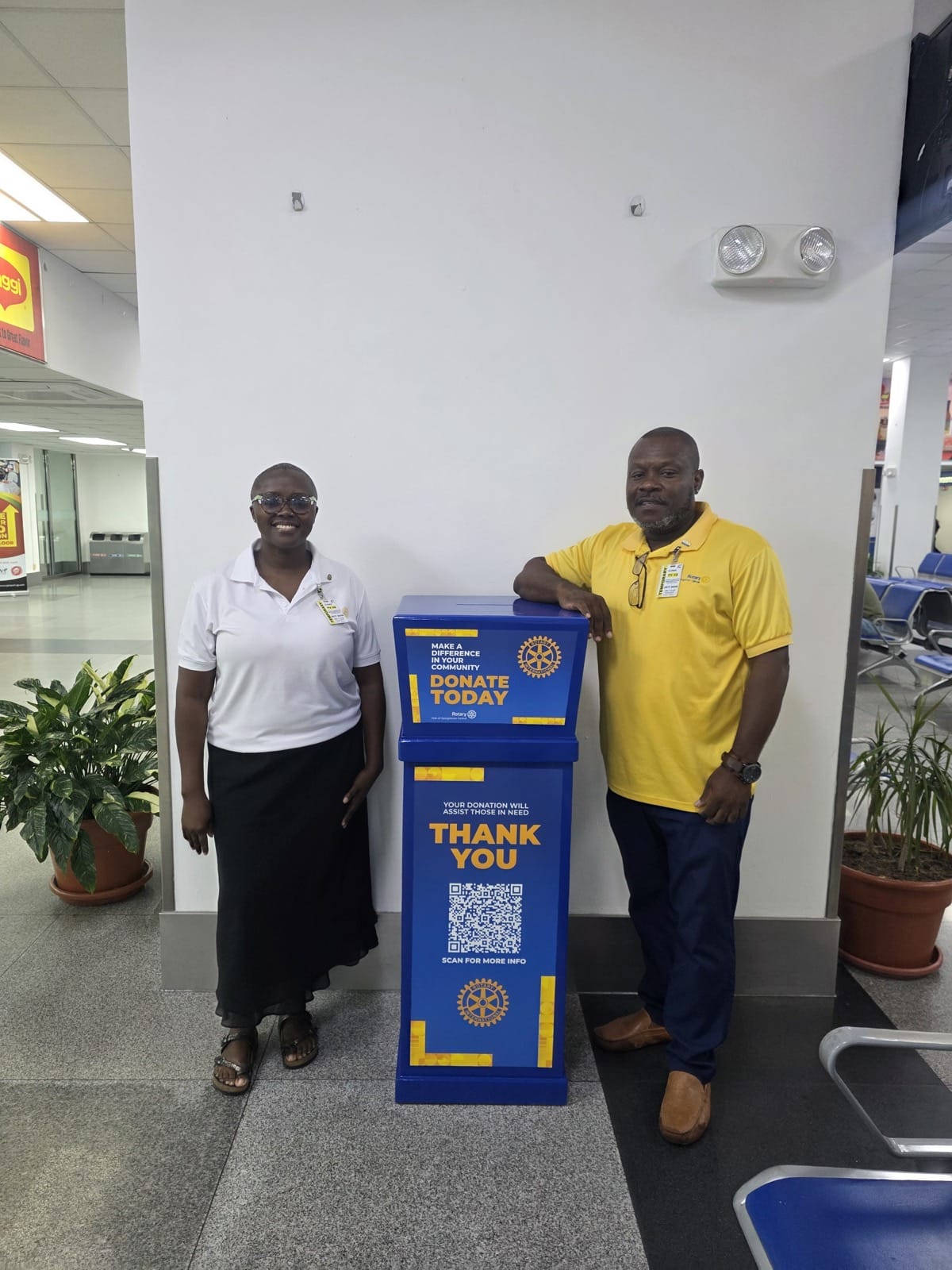 Michelle Howard, the club's Administration Chair, and Keon Howard, its Fundraising Chair, with the Change for Community box in the departure lounge at Cheddi Jagan International Airport