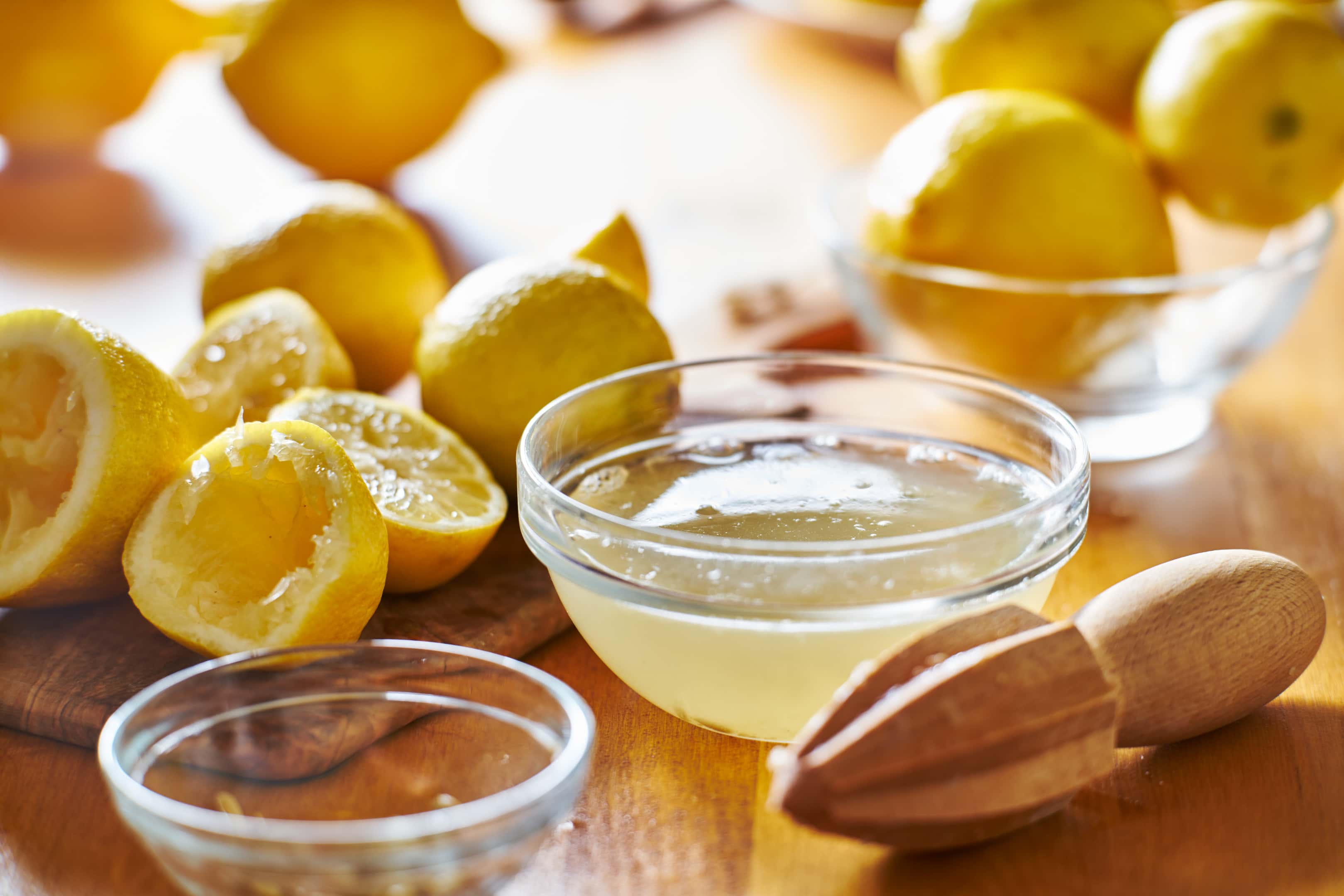Bowl of freshly squeezed lemon juice with wooden reamer on wooden table
