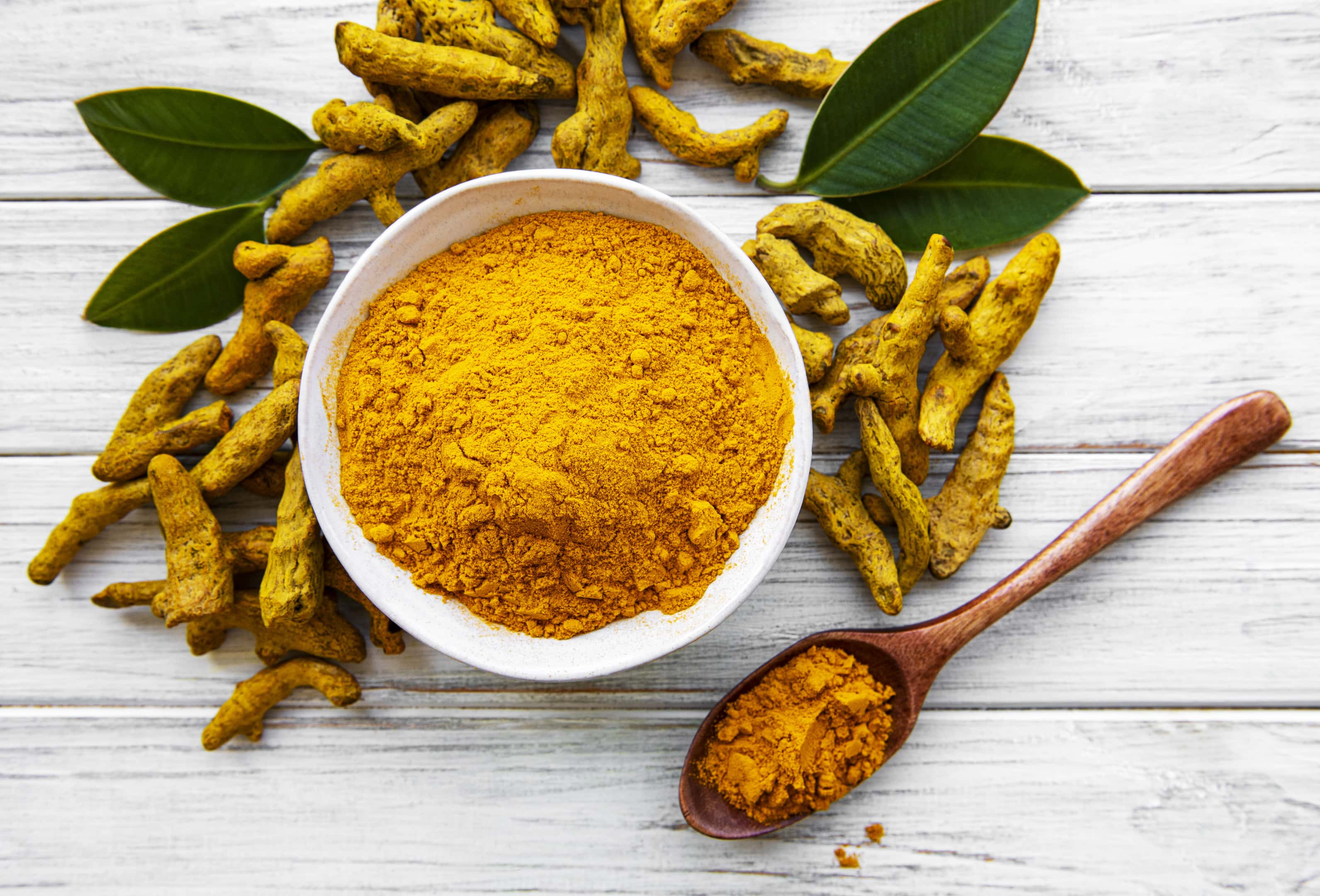 Bowl With Turmeric Powder and Dry Turmeric Roots on Wooden Surface