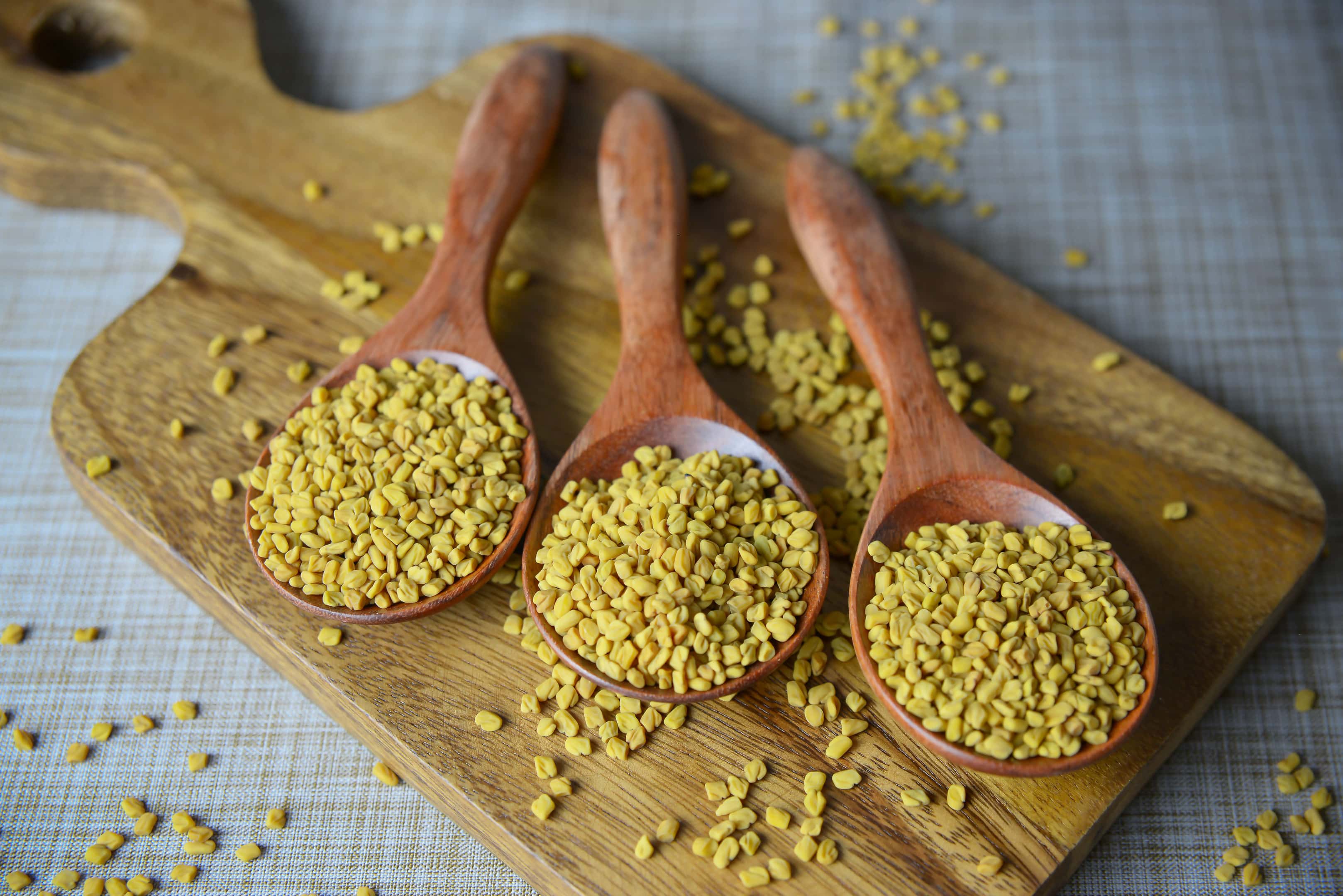 Fenugreek seeds in wooden spoons on wooden board