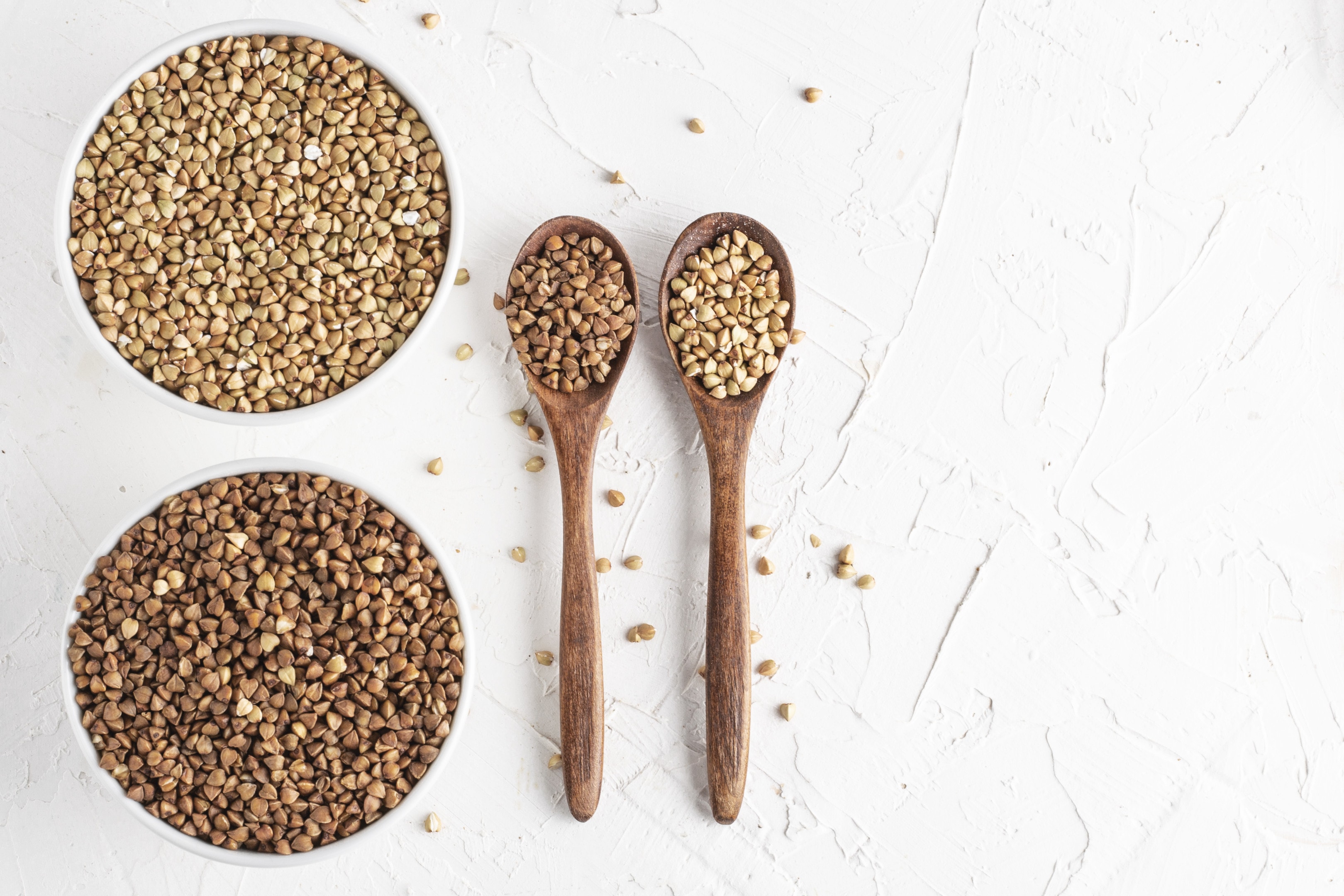 Green buckwheat and plain buckwheat with two wooden spoons on white background