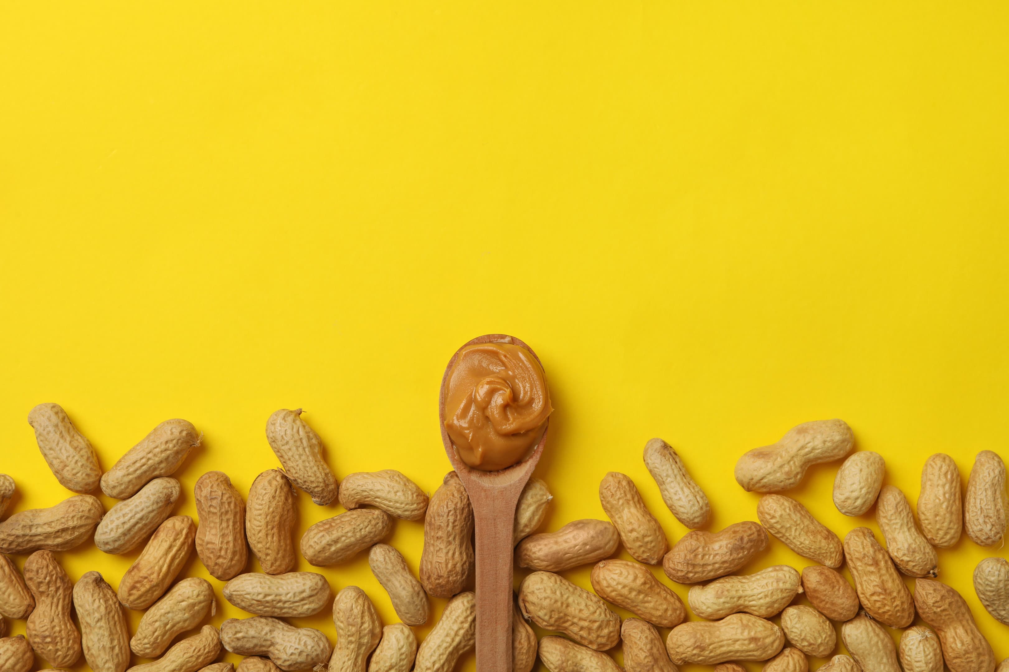 Peanut and spoon with peanut butter on yellow table
