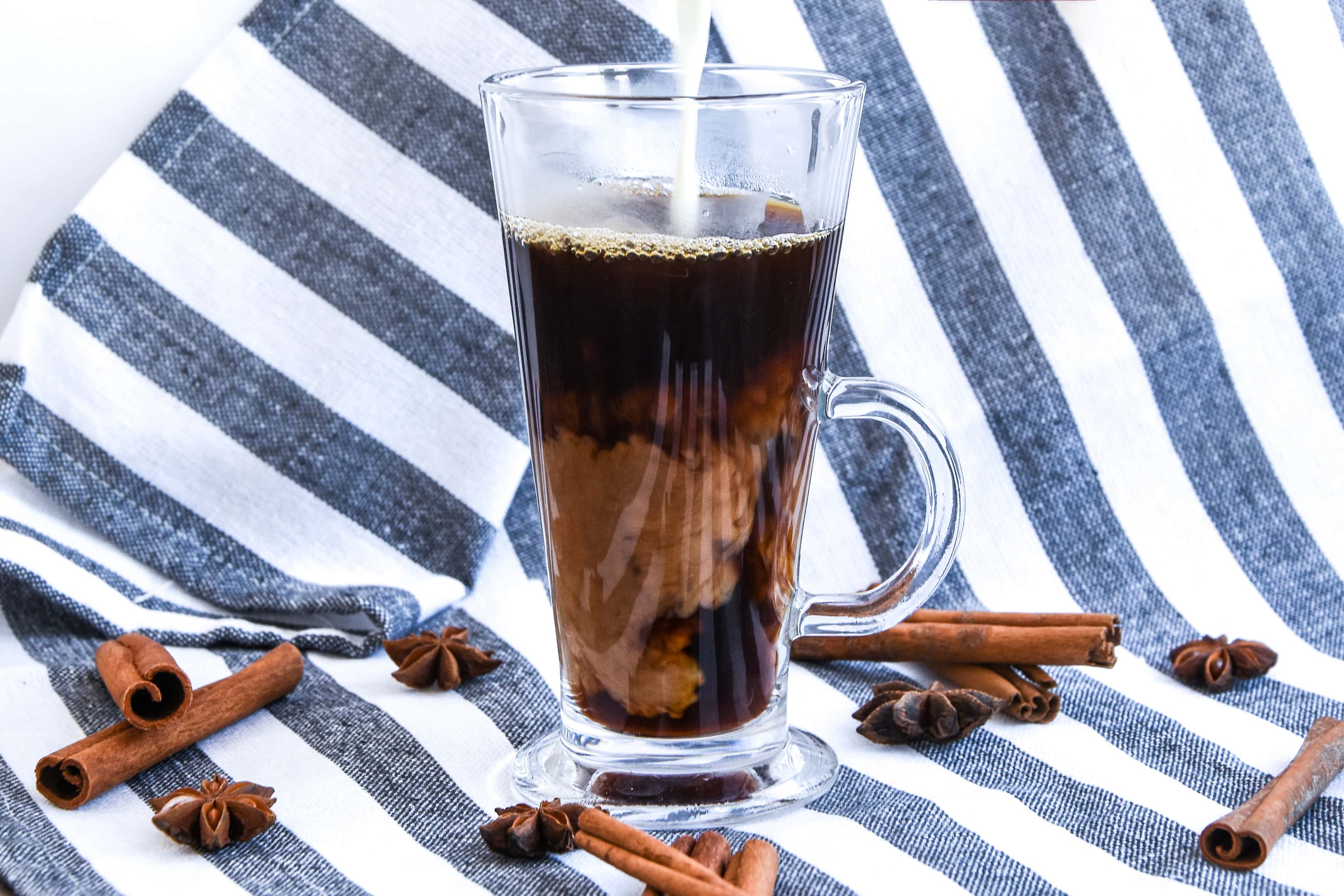 Pouring coffee creamer into glass with black coffee