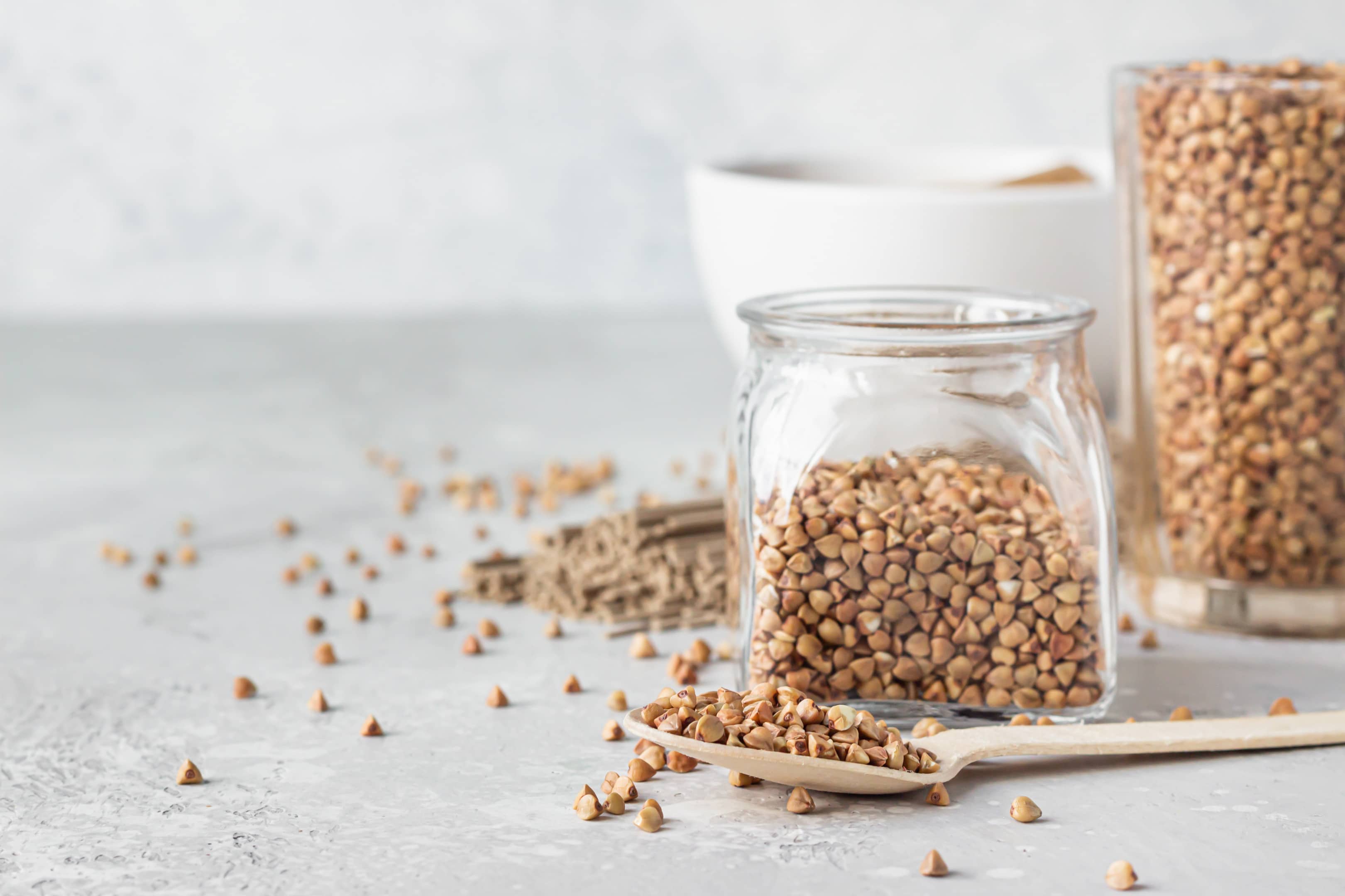 Uncooked buckwheat grains in glasses and wooden spoon