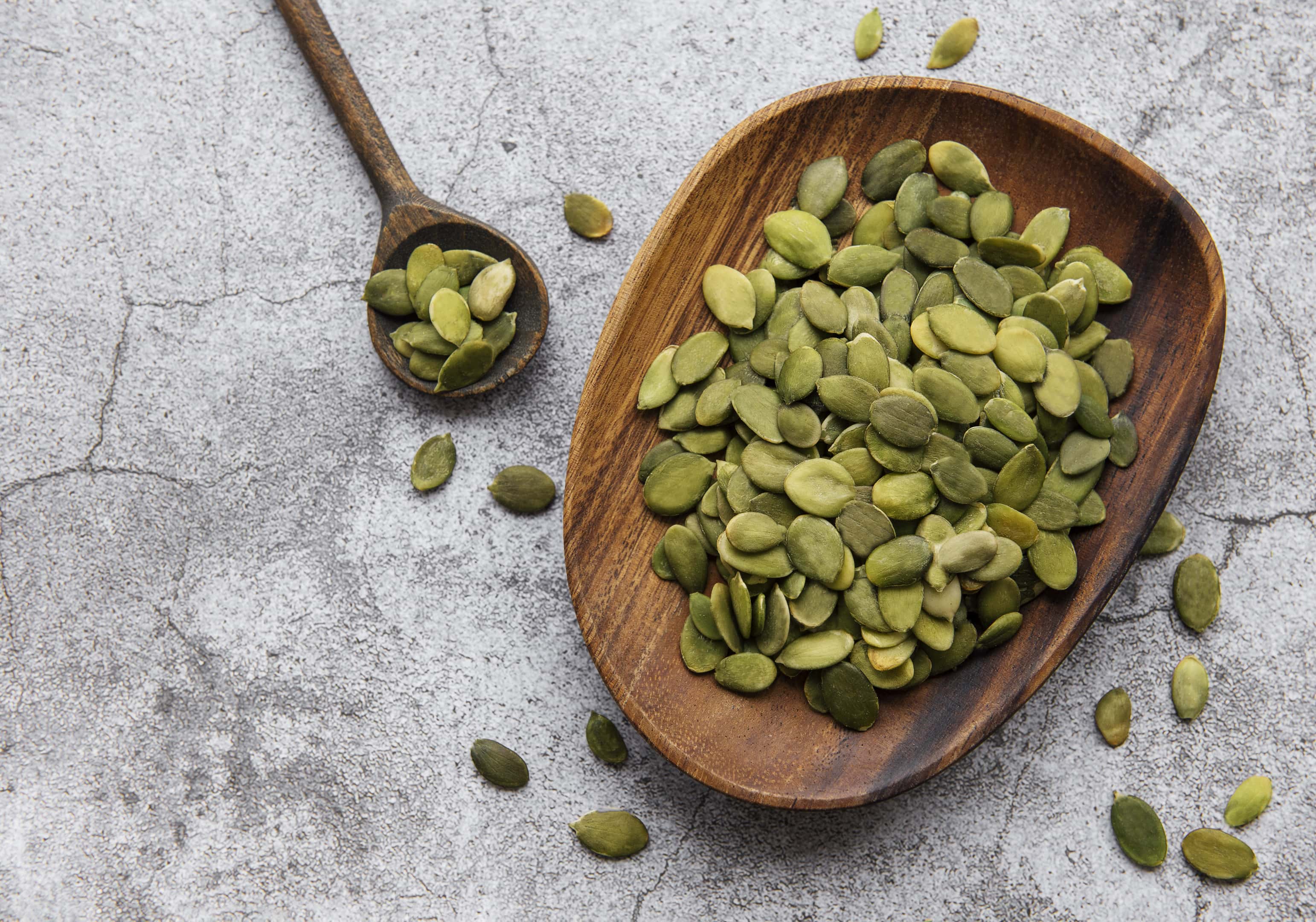 Wooden plate with pumpkin seeds on a gray concrete table