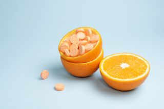 Half orange and peel with vitamin C tablets on a blue background