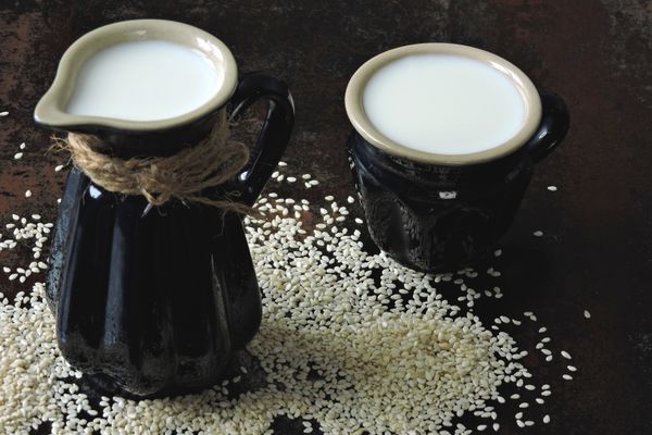 Sesame milk in jug and mug with scattered sesame seeds