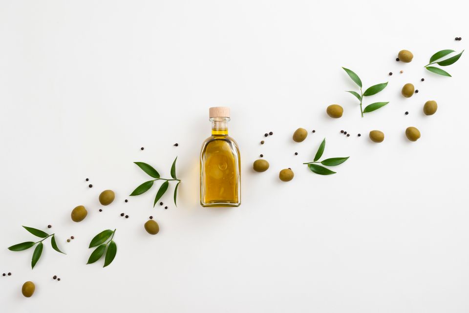 Arrangement of olive leaves and olive oil bottle on white background