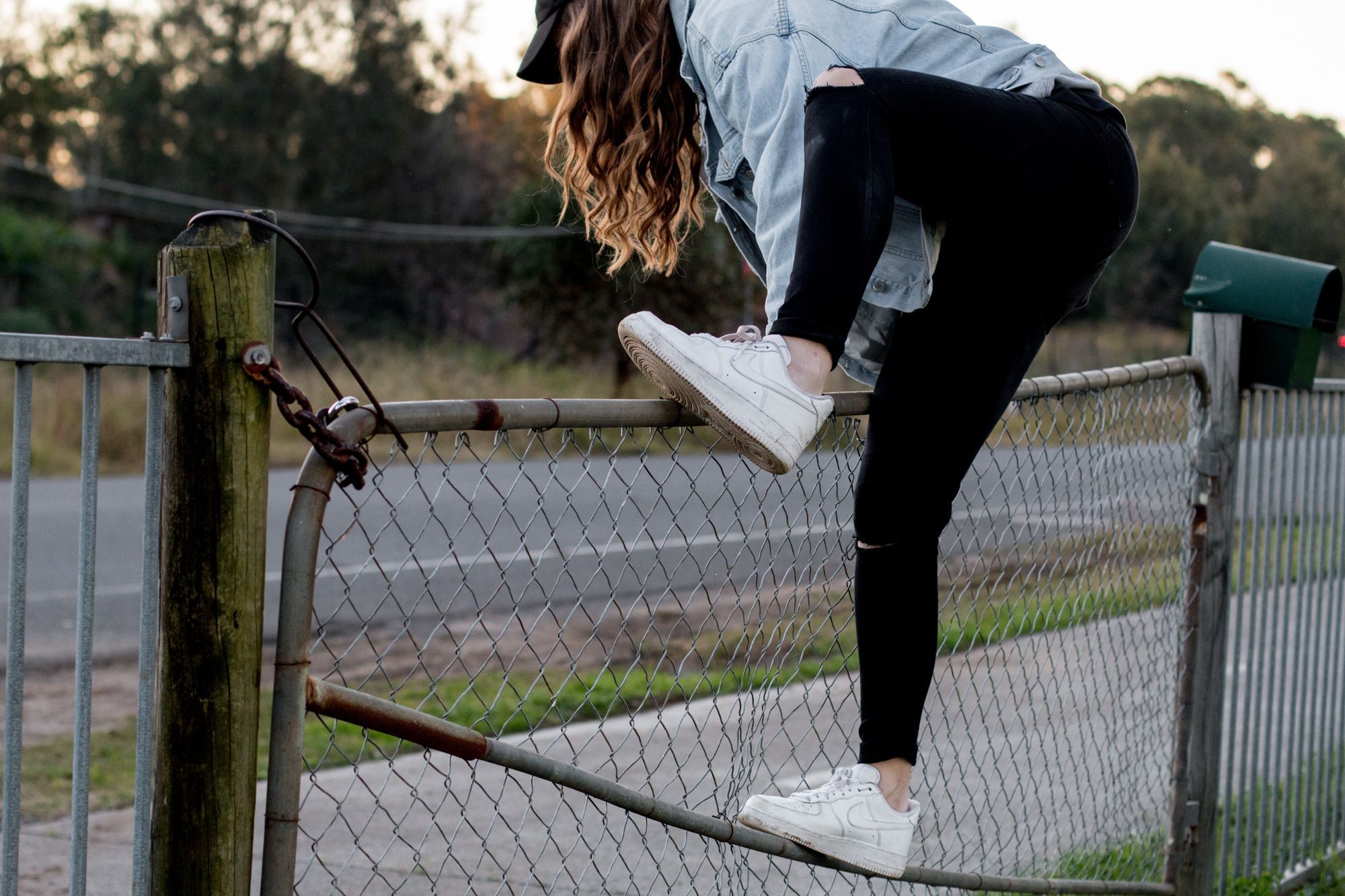 Someone in a jean jacket, sneakers, and leggings climbing over a locked and chained fenc