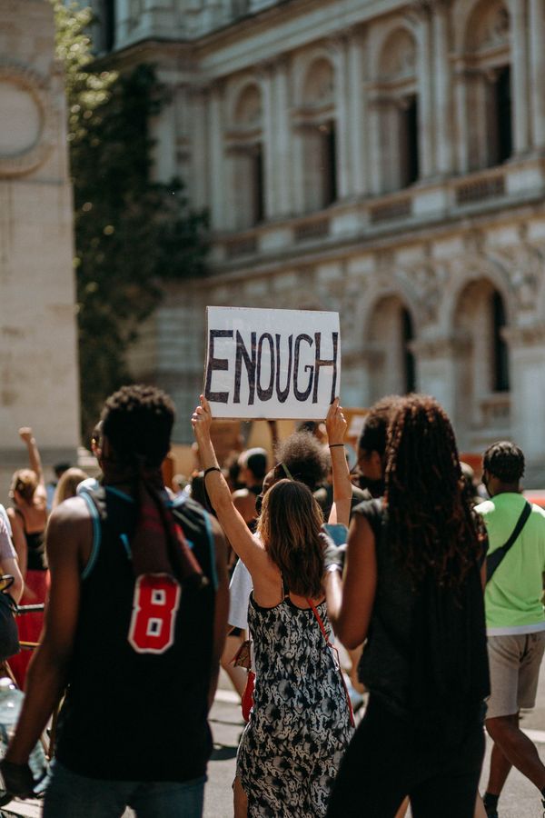 Protest photo, no faces shown, marching down a road. A sign that says ENOUGH is held high.