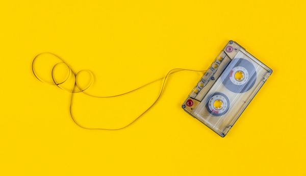 A cassette tape on a yellow background with some of its tape pulled out and looped around.