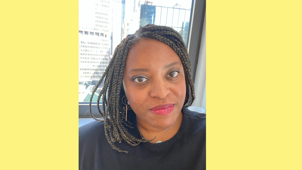 Headshot of Aimi Knowling in front of the window; you can see New York skyscrapers behind her.
