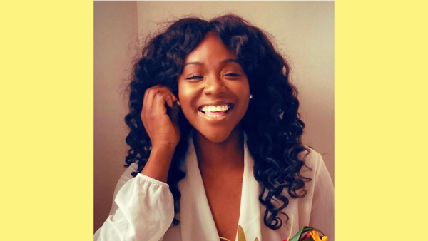 Aziza, a Black woman with dark curly hair, smiles and laughs at the camera.
