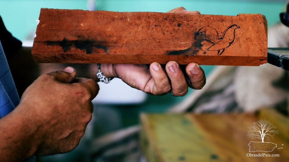 Carlos sostiene un bloque de madera con el contorno de un gallo dibujado