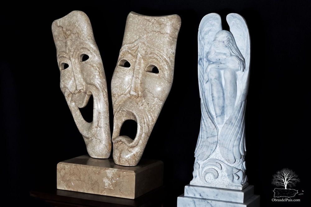 Dos máscaras de piedra sobre una base y una figura alada tallada en piedra clara.