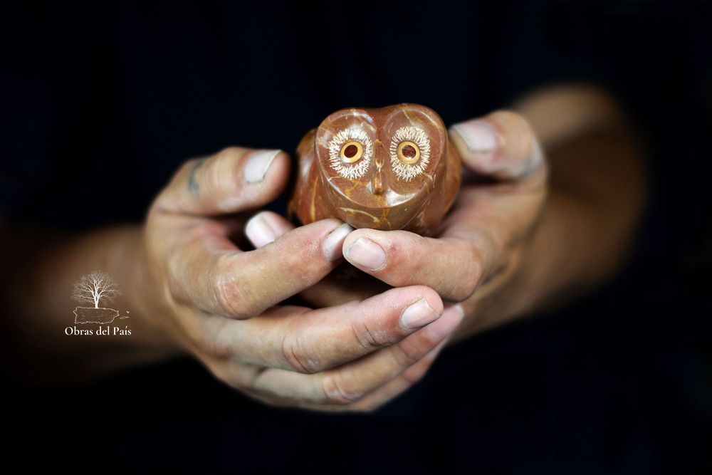 Manos sosteniendo una pequeña lechuza tallada en piedra de tonos marrones.