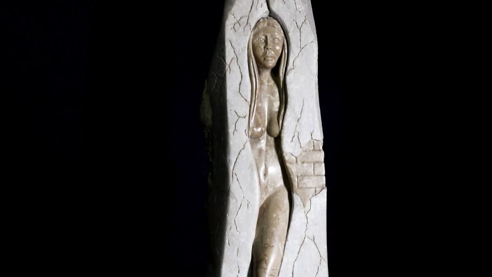 Figura femenina tallada en piedra dentro de una estructura vertical con grietas visibles.